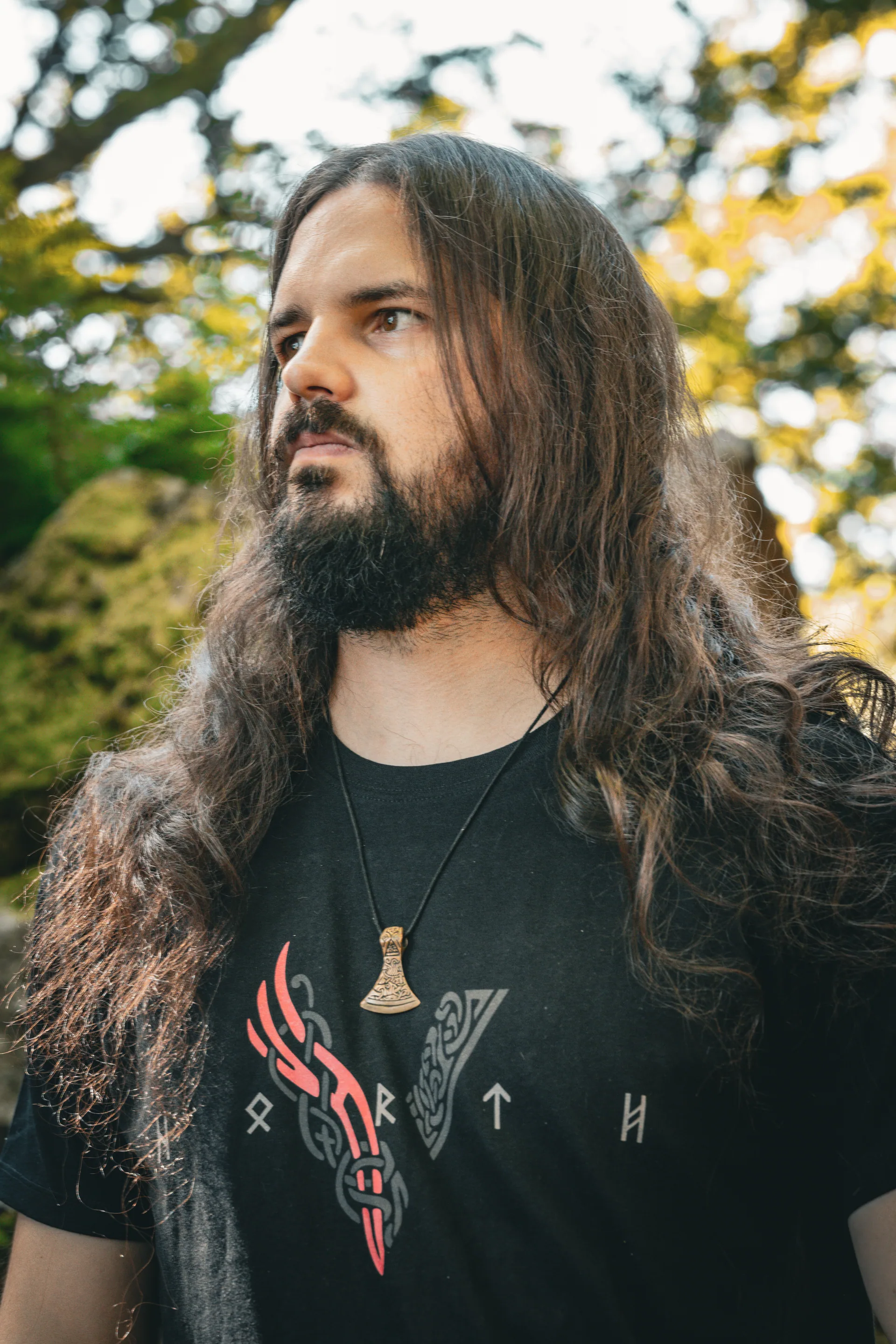 Mann mit langen Haaren und Bart im Wald, trägt North Legendary Äxte-Shirt mit rotem Print