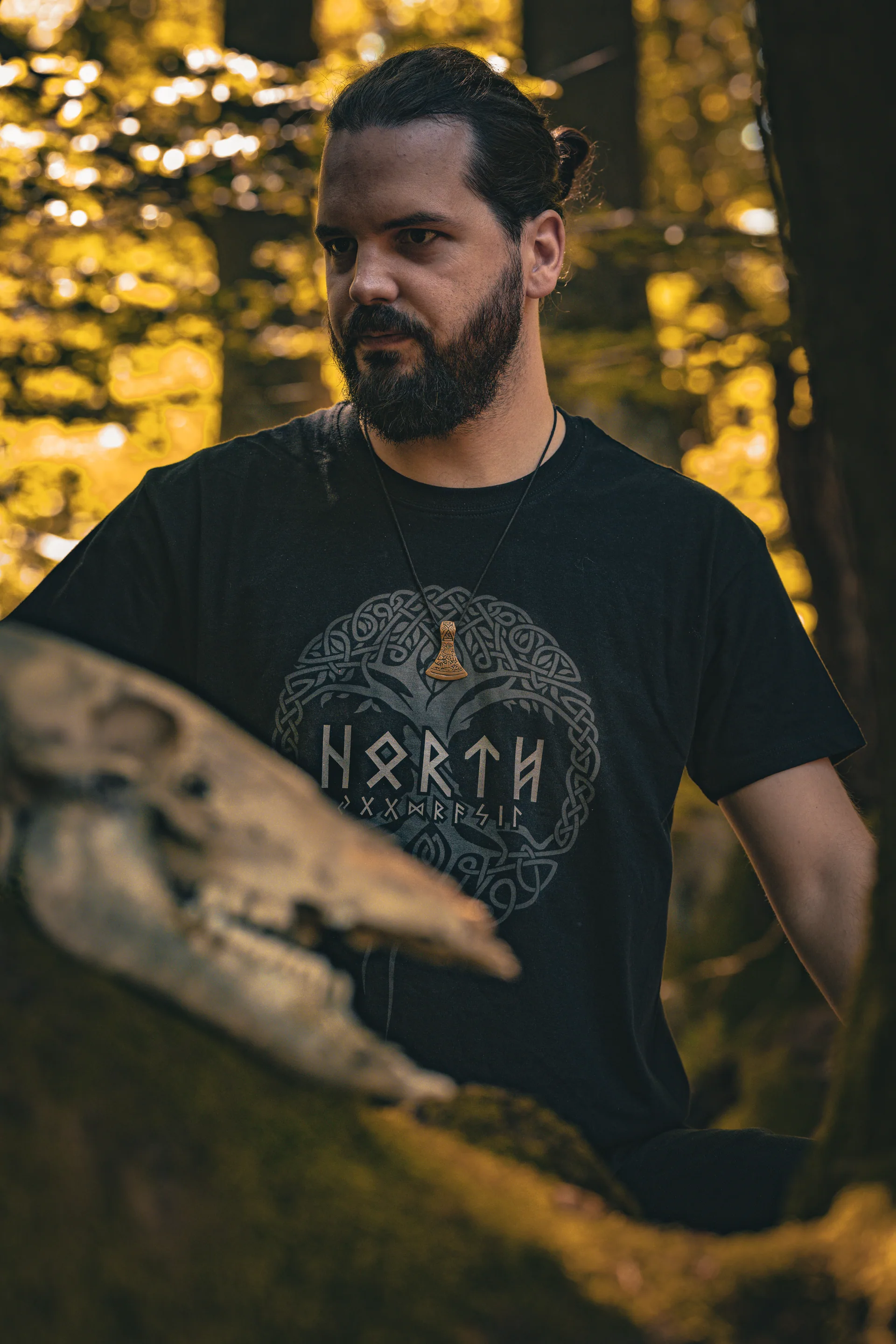 Mann mit Dutt im Wald, trägt North Legendary Yggdrasil-Shirt, hält einen Tierschädel im Vordergrund