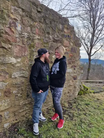 Paar in North Legendary Hoodies vor einer mittelalterlichen Burgruine, lachender Blickkontakt